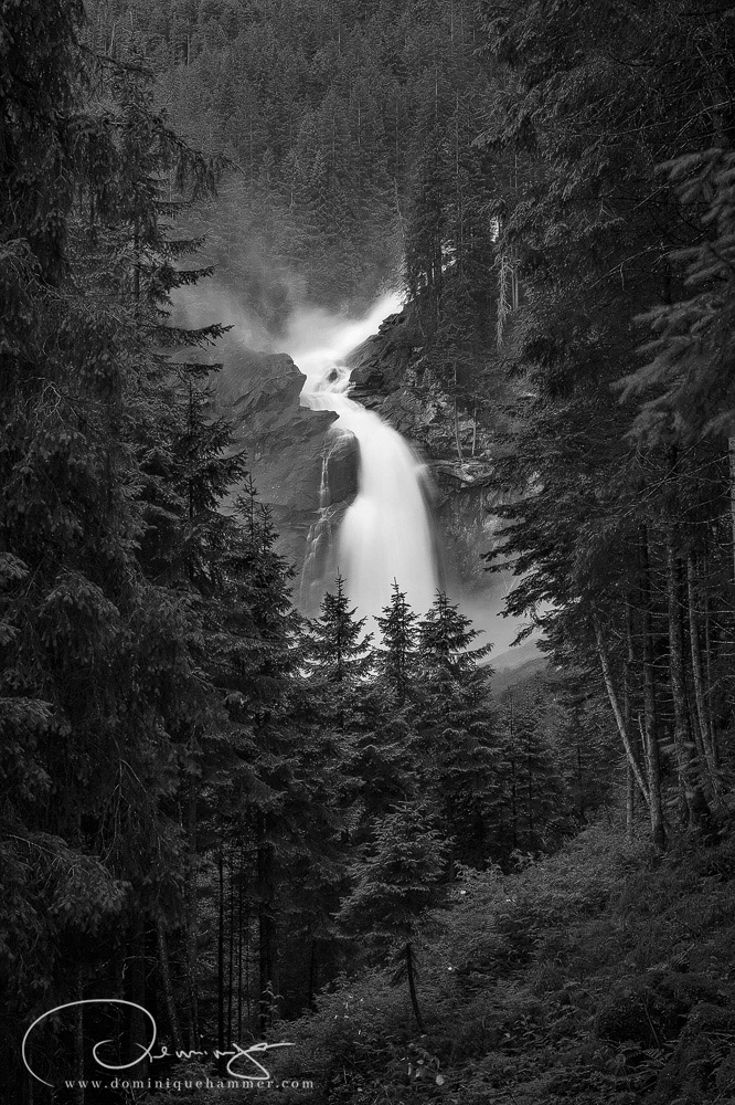 Eine schwarz weiss Aufnahme des Krimmler Wasserfalls ungeben von B&auml;umen von Fotograf Dominique Hammer