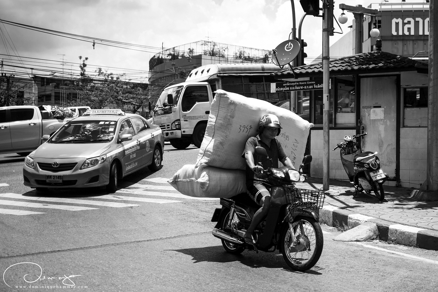 Ein Mann transportiert eine Matratze mit einem Motorrad auf den Stra&szlig;en von Bangkok von Fotograf Dominique Hammer